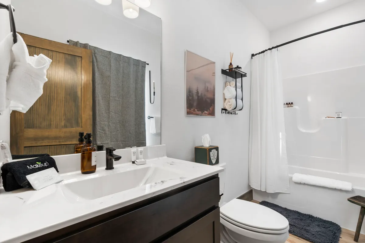 A modern, serene bathroom with a vanity and sink, a framed mirror, fresh towels on a rack, and tasteful wall art. The space is bright and calming, ideal for relaxation and daily routines.