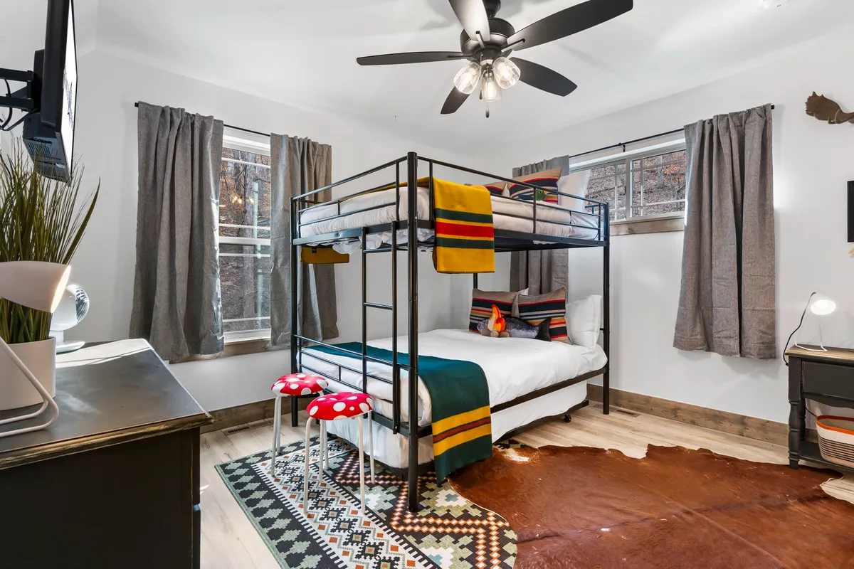 This inviting room includes a colorful bunk bed, playful mushroom stools, a soft area rug, and decorative blankets. The decor is whimsical, signaling a space where kids can play, read, or hang out together in comfort.