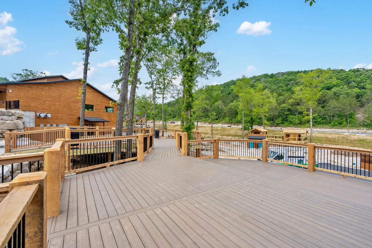 A spacious wooden deck set amidst lush surrounding trees, with distant hills visible beyond. The scene evokes serenity and outdoor relaxation, ideal for activities like strolling, relaxing, and gathering. The deck offers a seamless connection to the natural environment, suggesting a welcoming spot for both guests and their pets to unwind and enjoy the fresh air.