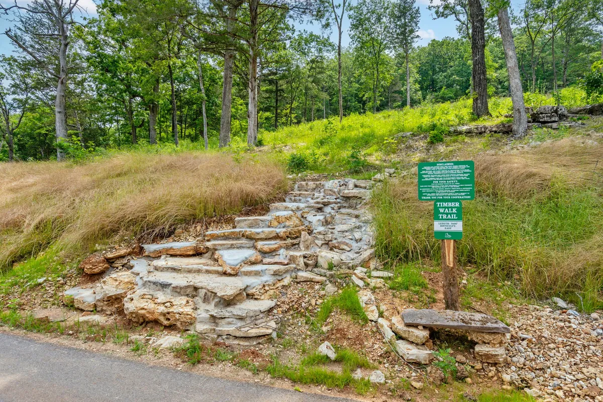A trailhead with natural stone steps and a wooden sign, surrounded by lush greenery, invites exploration and adventure just beyond the cabin. The scene feels both inviting and full of potential for nature walks.