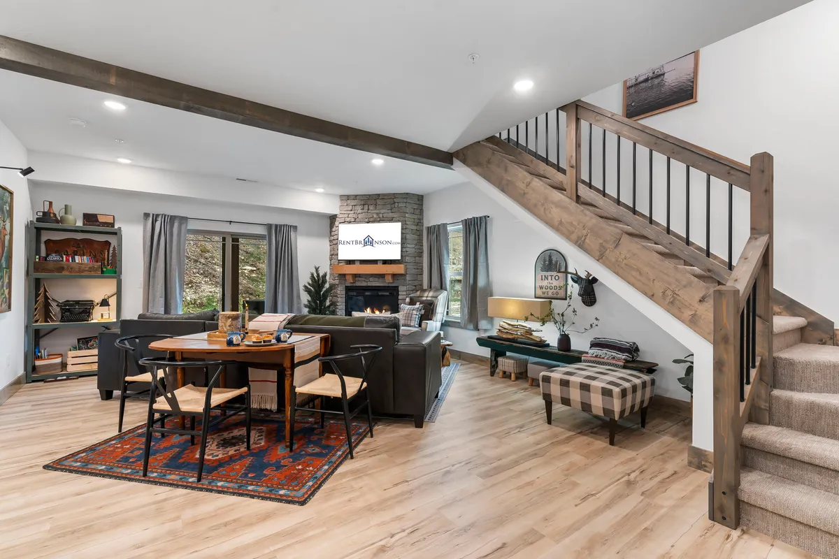 A cozy dining area with a substantial table, a warm fireplace, and a staircase in the background. The space is illuminated with soft lighting, encouraging family meals and celebrations.