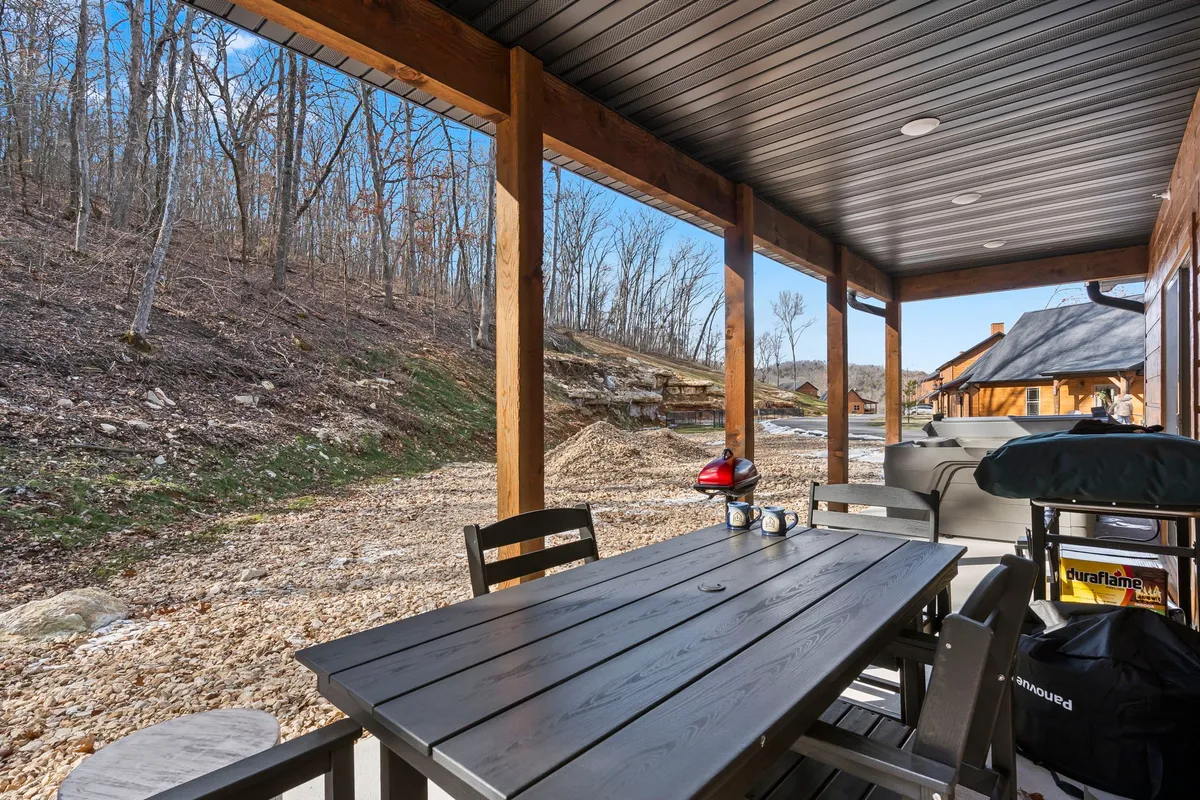 An inviting outdoor patio with a wooden dining table, surrounded by natural landscape and featuring an outdoor grill. The setting is ideal for al fresco dining, barbecues, and enjoying nature.