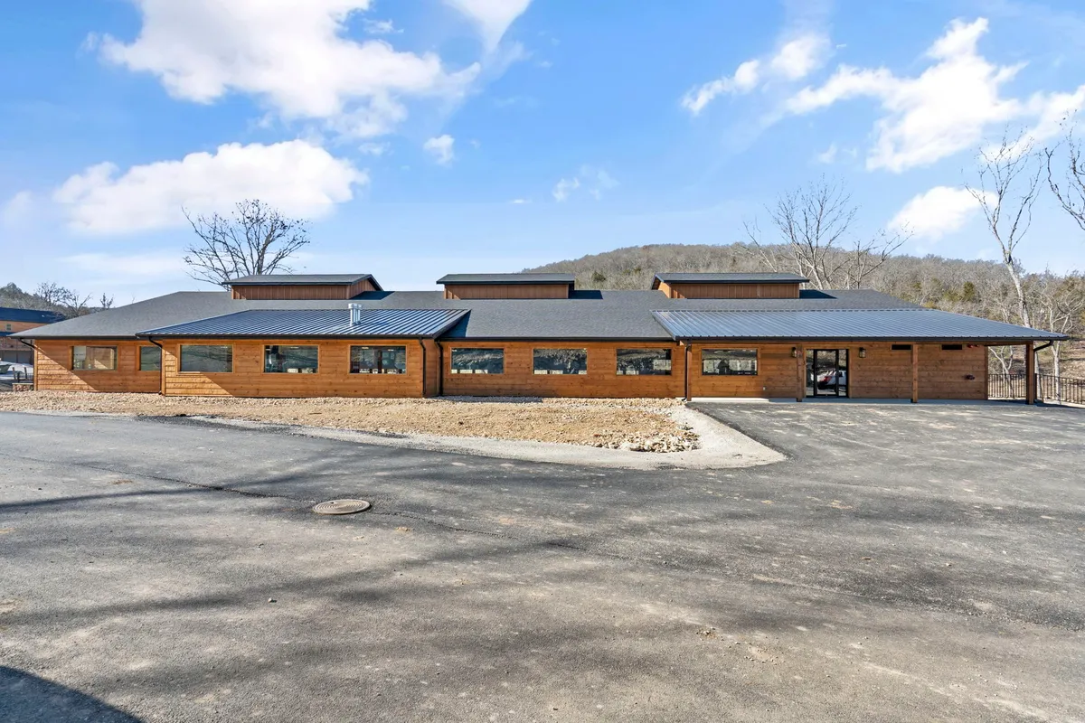 This image features the exterior of a newly built wooden lodge with a welcoming facade, large windows, and a sleek metal roof. The environment is serene, with room for families to gather on the porch, watch the sunrise, or stargaze at night.