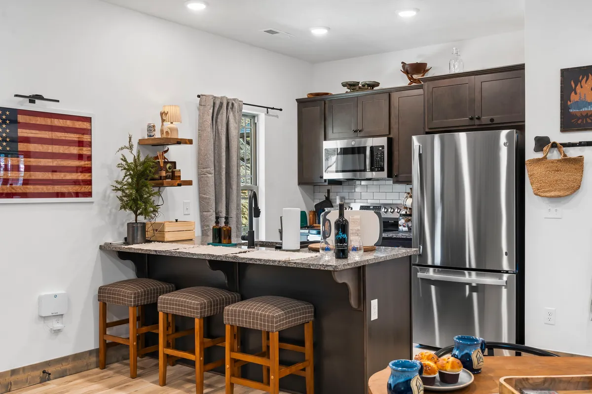 A welcoming kitchen with a central island featuring stool seating, modern appliances, and flag artwork on the wall. The space has an inviting, homey feel, perfect for cooking together or gathering for meals.